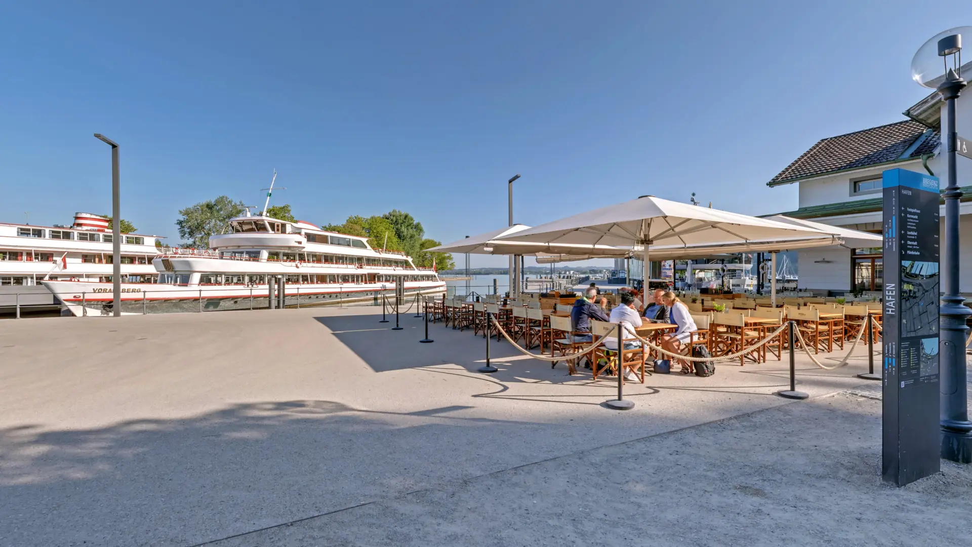 Hafen mit Restaurant und vorbeifahrendem Schiff.