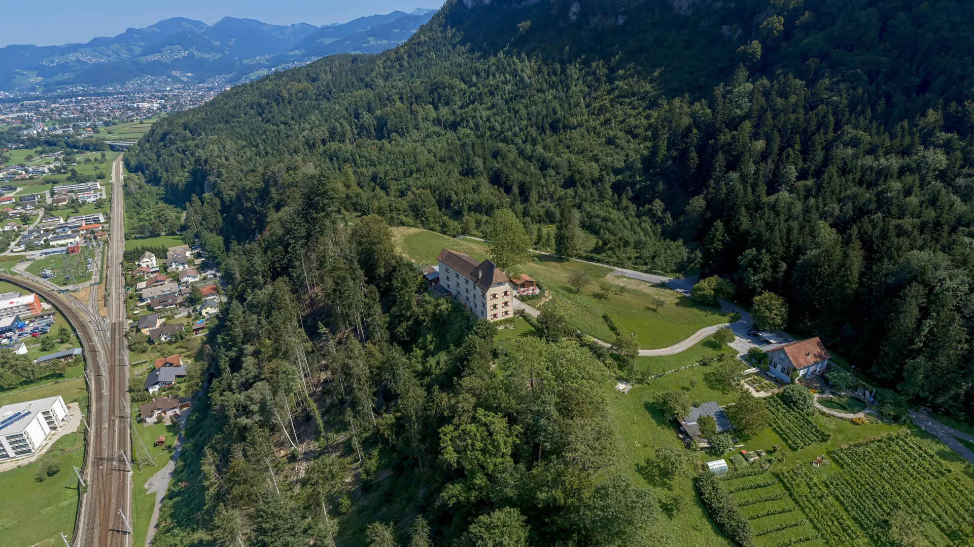 Luftaufnahme von Gebäuden in hügeliger Waldlandschaft.