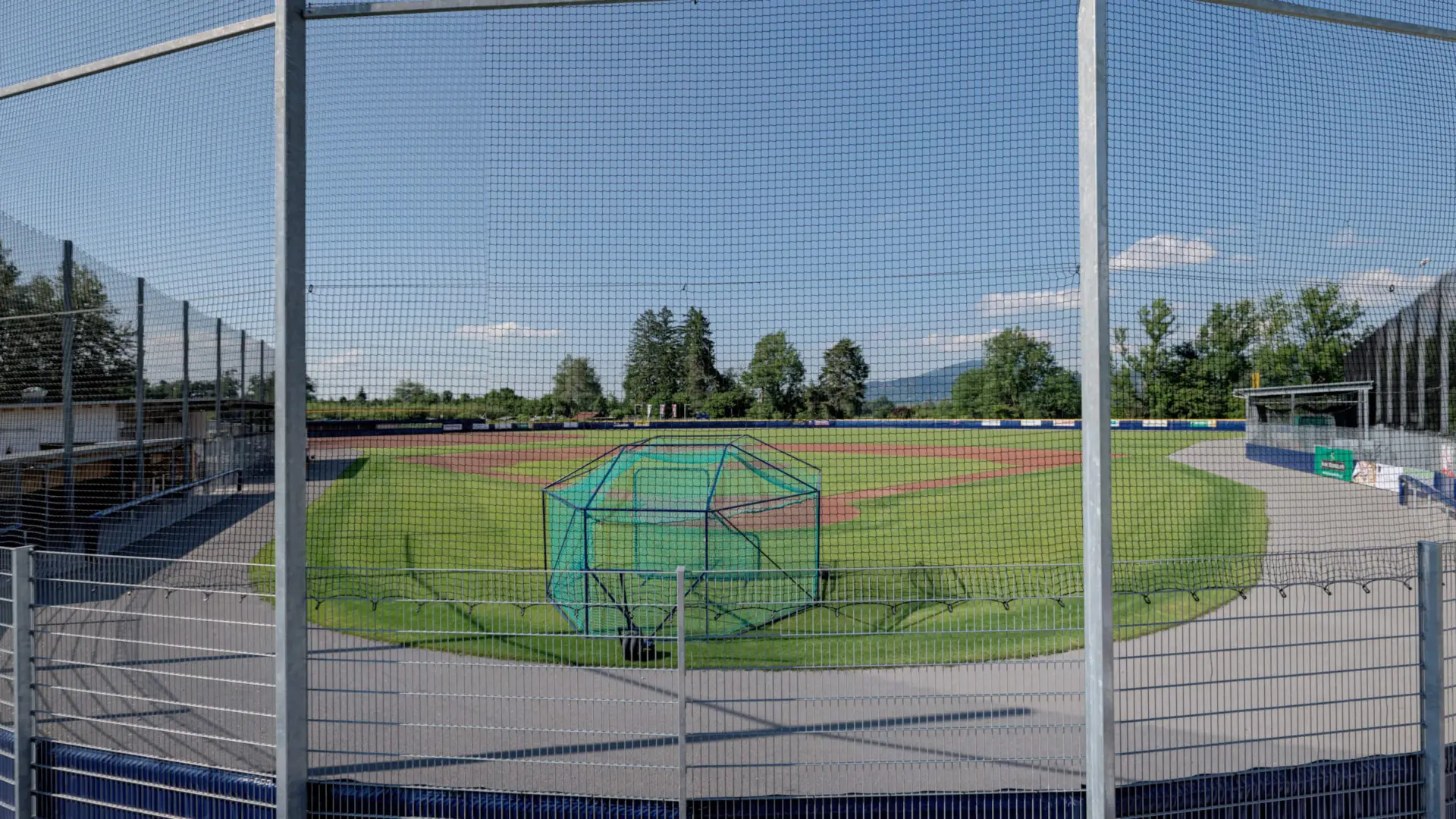 Baseballfeld bei sonnigem Wetter, hinten Bäume