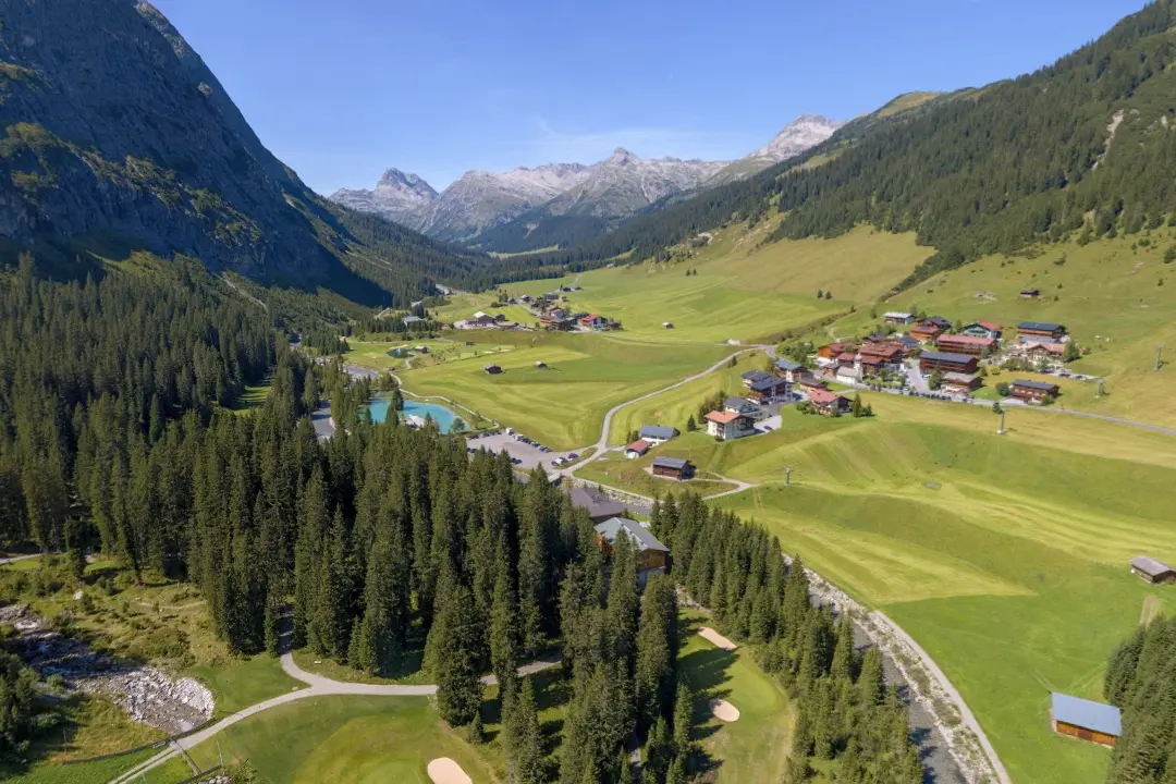 Alpenlandschaft mit Wiesen, Wald und Gebäuden.