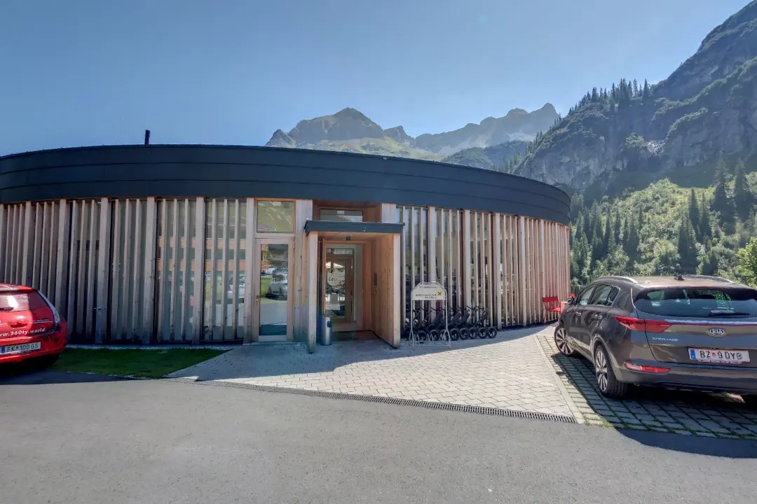 Rundes Holzgebäude mit Autos und Bergen im Hintergrund.