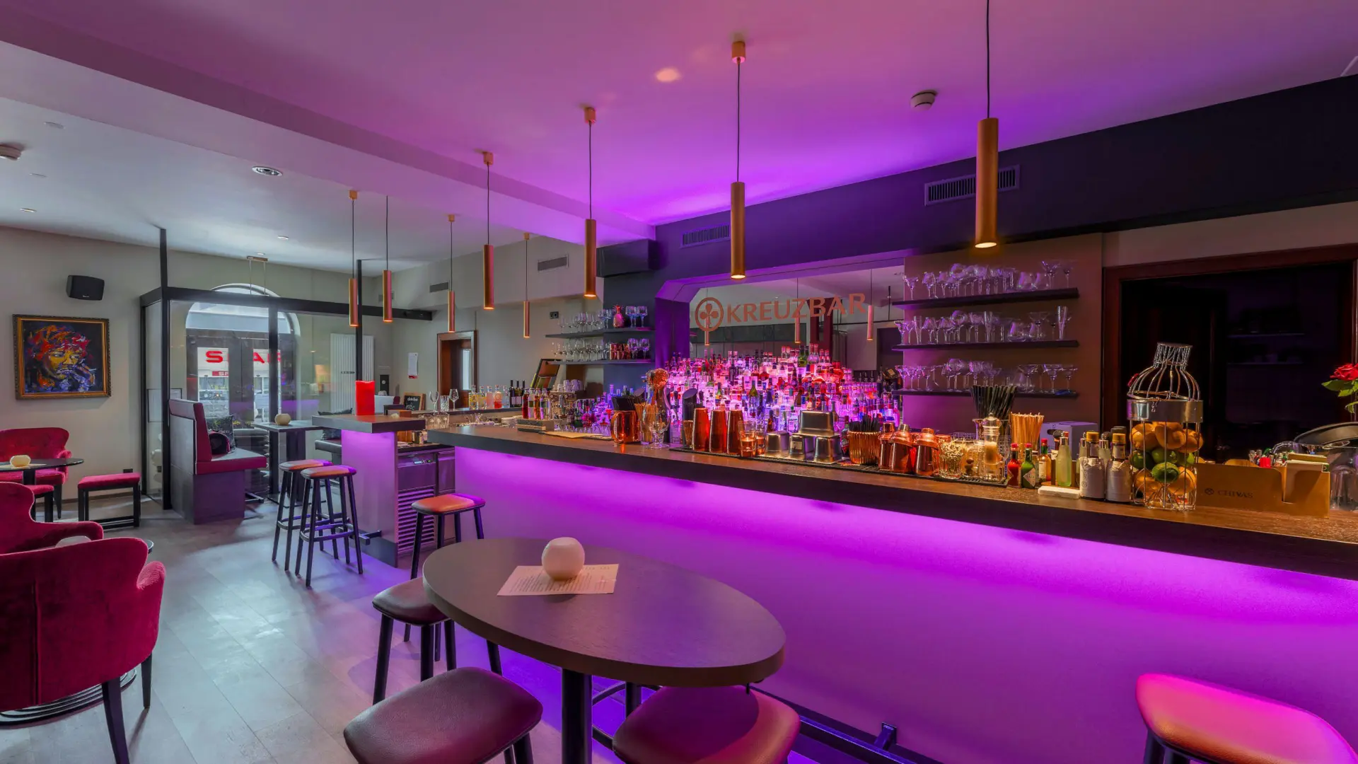 Moderne Bar mit lila Beleuchtung und Sitzmöglichkeiten.