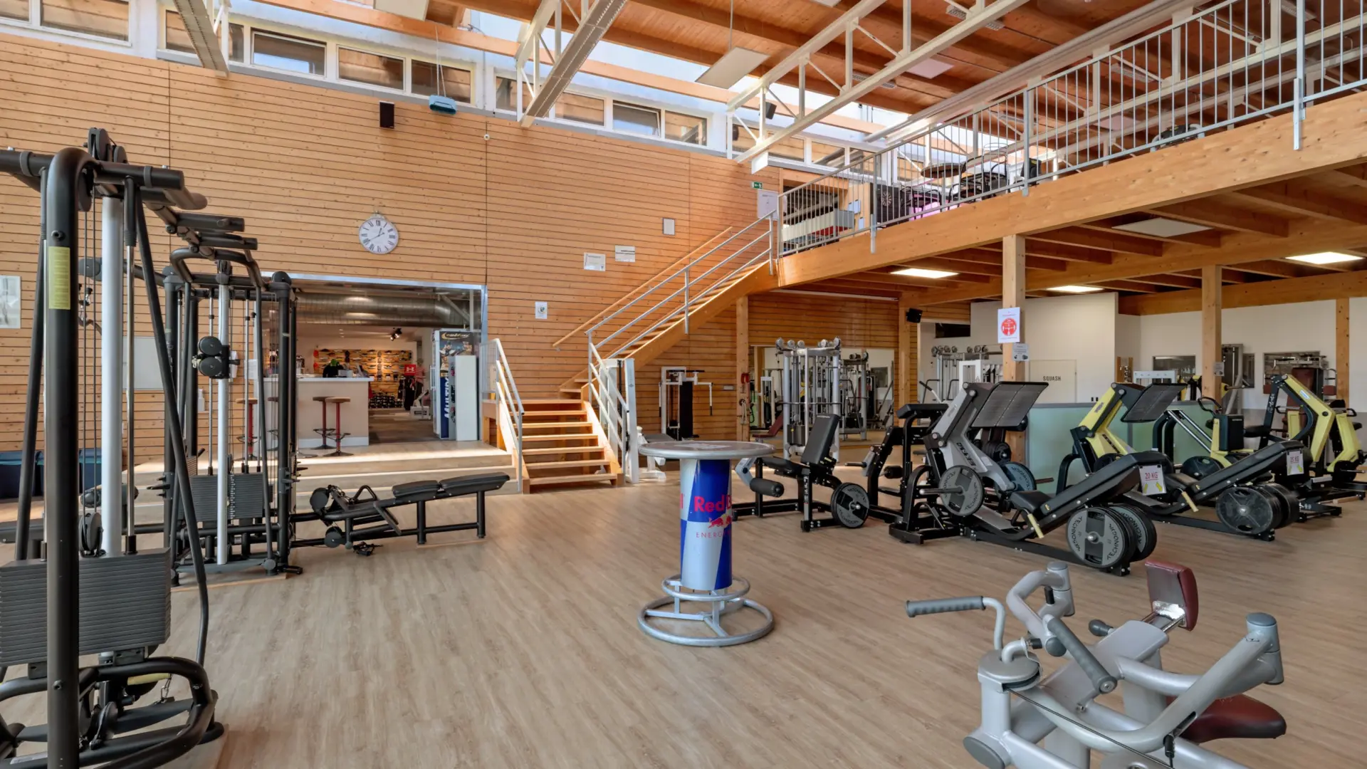 Helles Fitnessstudio mit modernen Geräten und Holzverkleidung.
