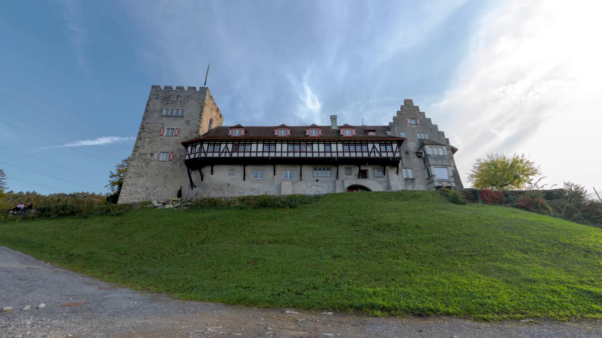 Historische Burg auf grüner Anhöhe unter blauem Himmel.