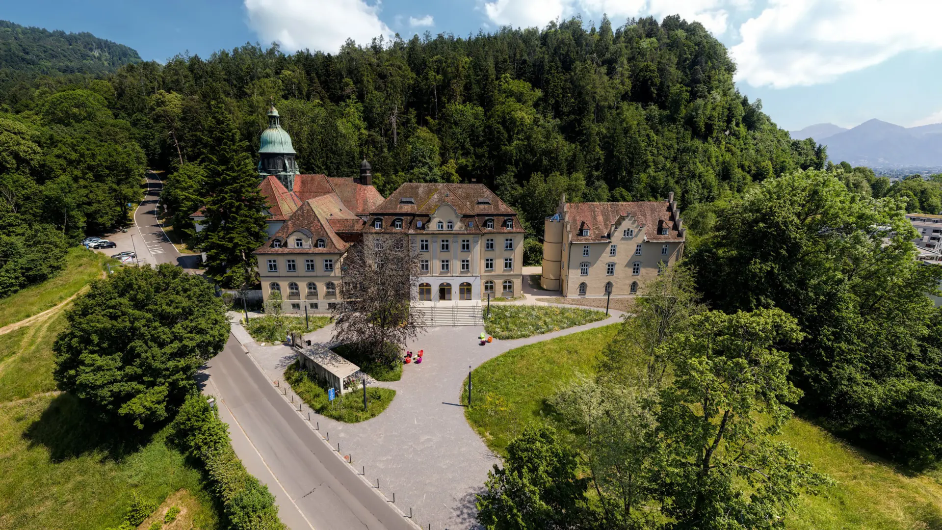 Historisches Gebäude im Grünen mit bewaldetem Hintergrund.
