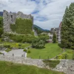 Alte Burgruine mit Garten und Bergen im Hintergrund.