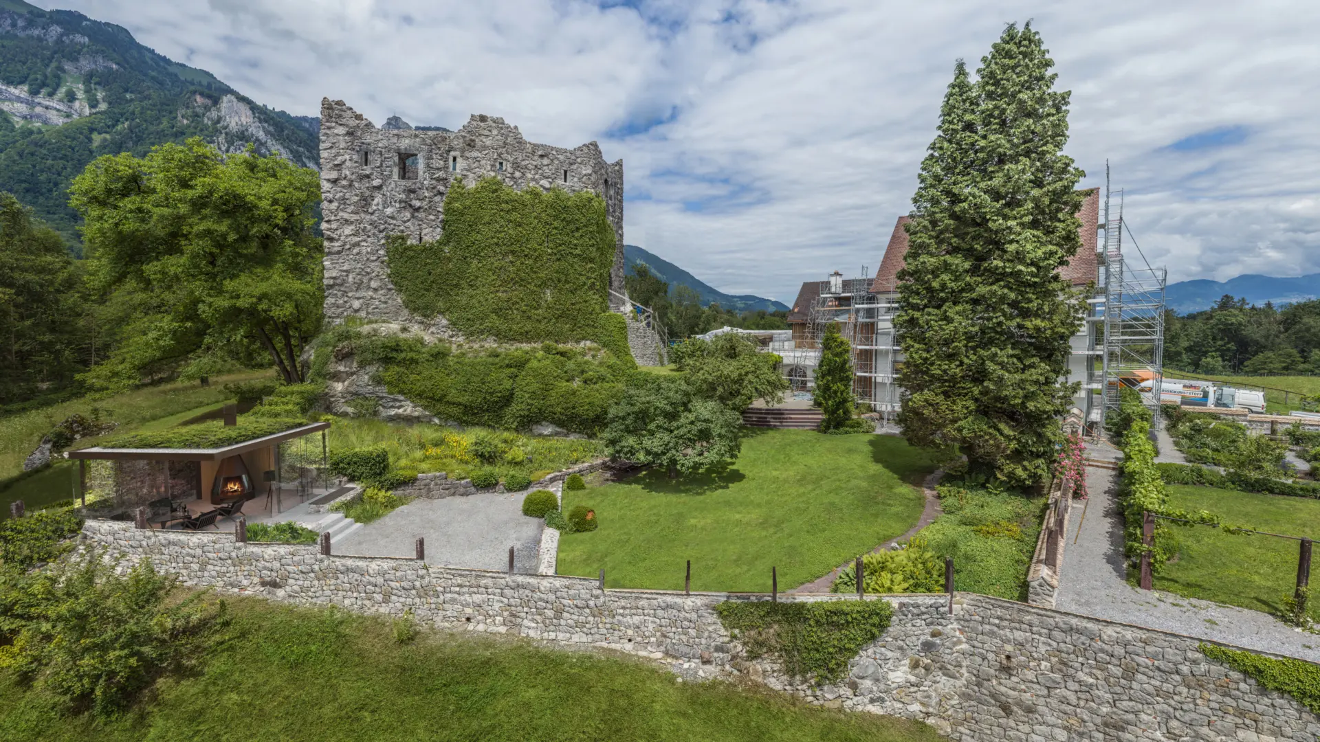 Alte Burgruine mit Garten und Bergen im Hintergrund.