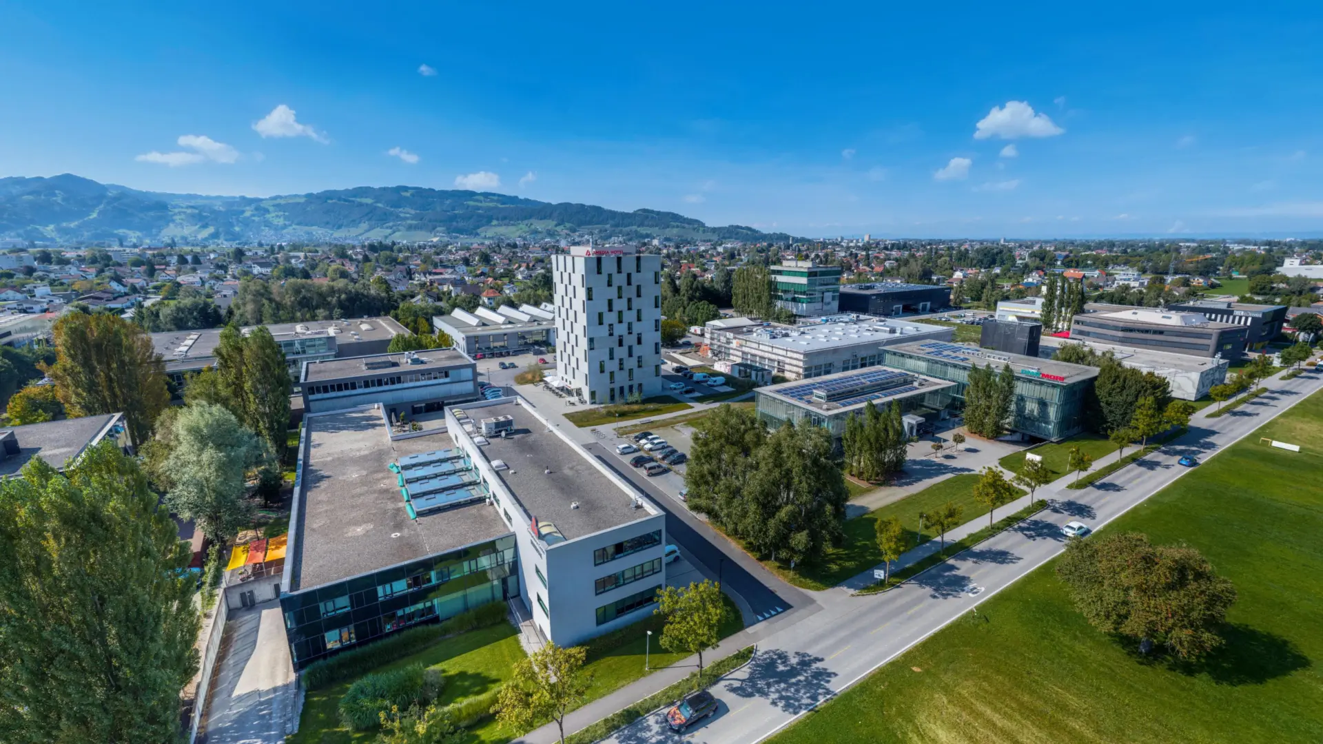 Gebäudeensemble im Grünen mit Hügeln im Hintergrund.
