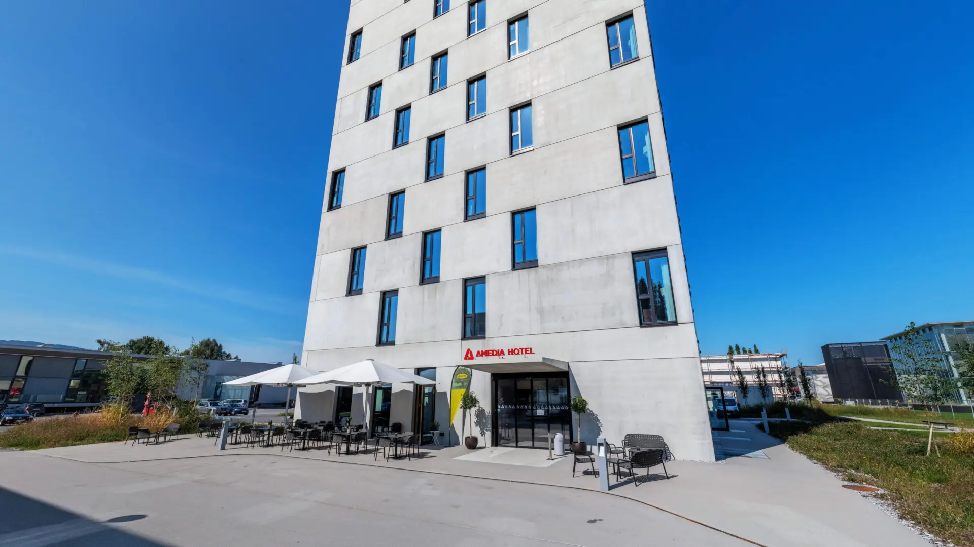 Modernes Hotel mit Außensitzbereich unter Sonnenschirmen.