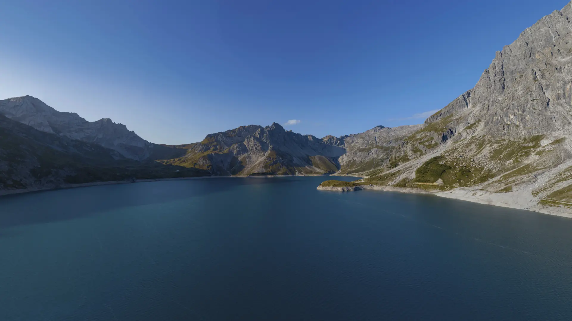 Bergsee mit umgebenden Gebirgsformationen und blauem Himmel.