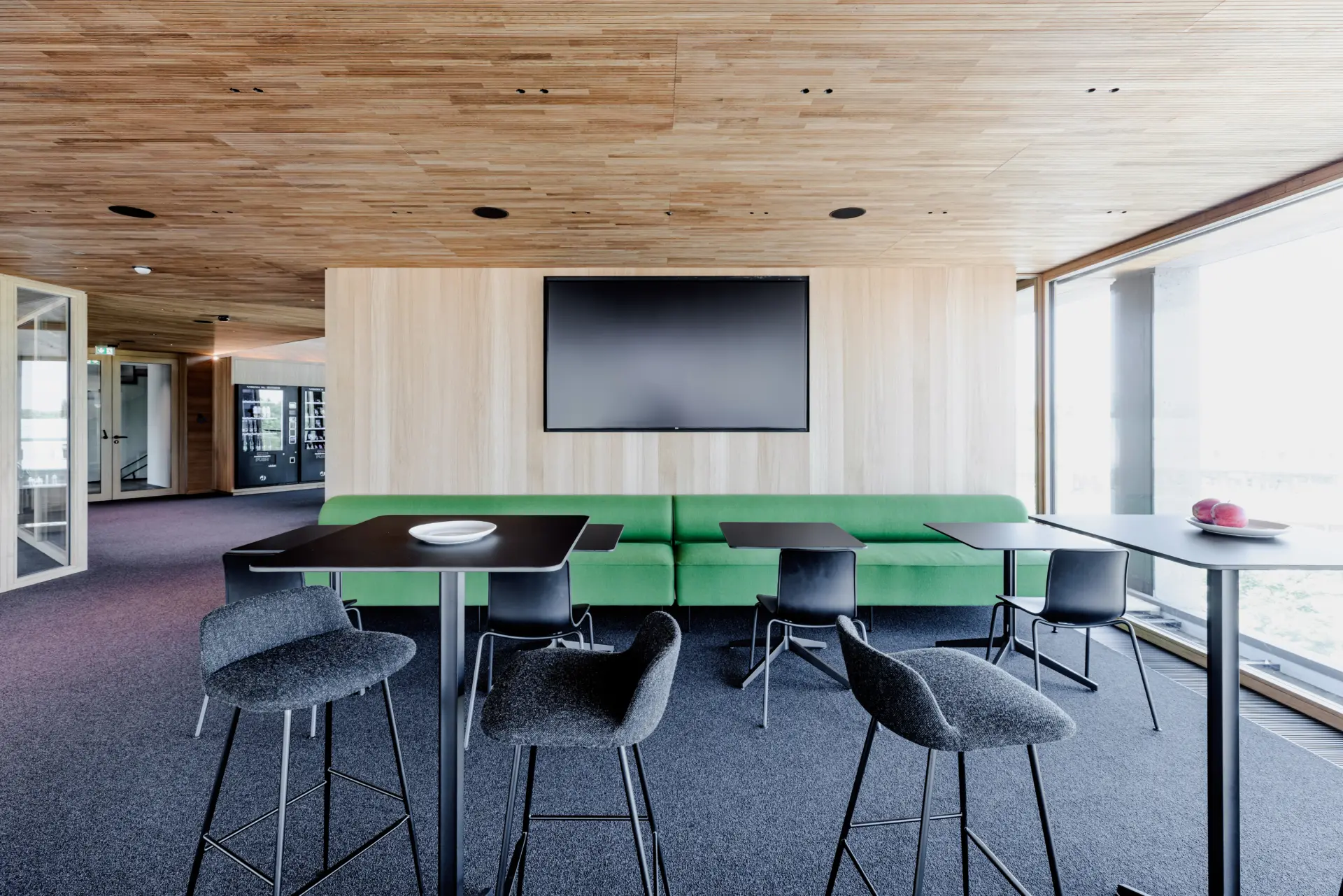 Moderne Cafeteria mit grüner Couch und Tischen.