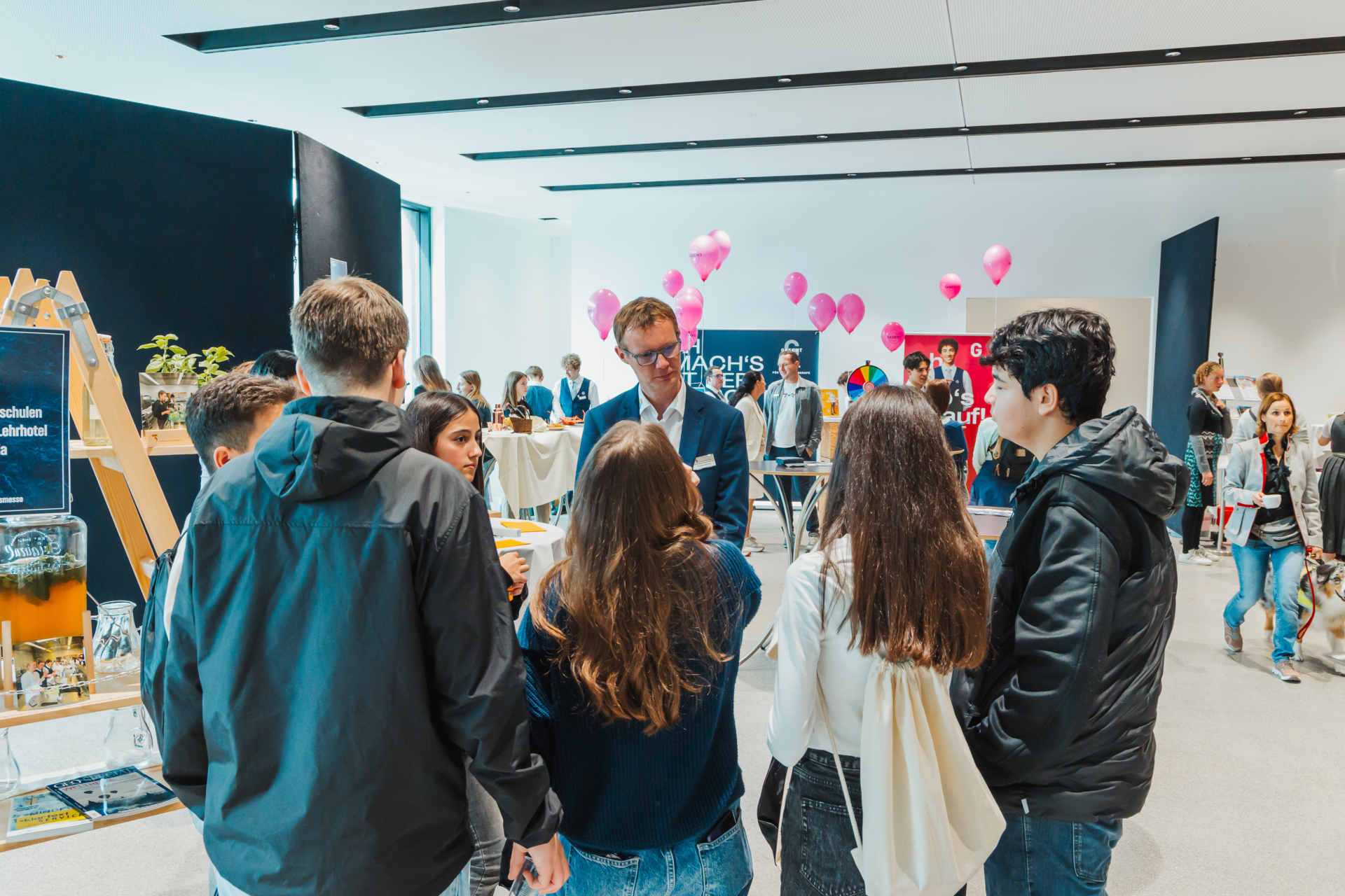 Personengruppe bei Messe mit Infoständen und Luftballons.