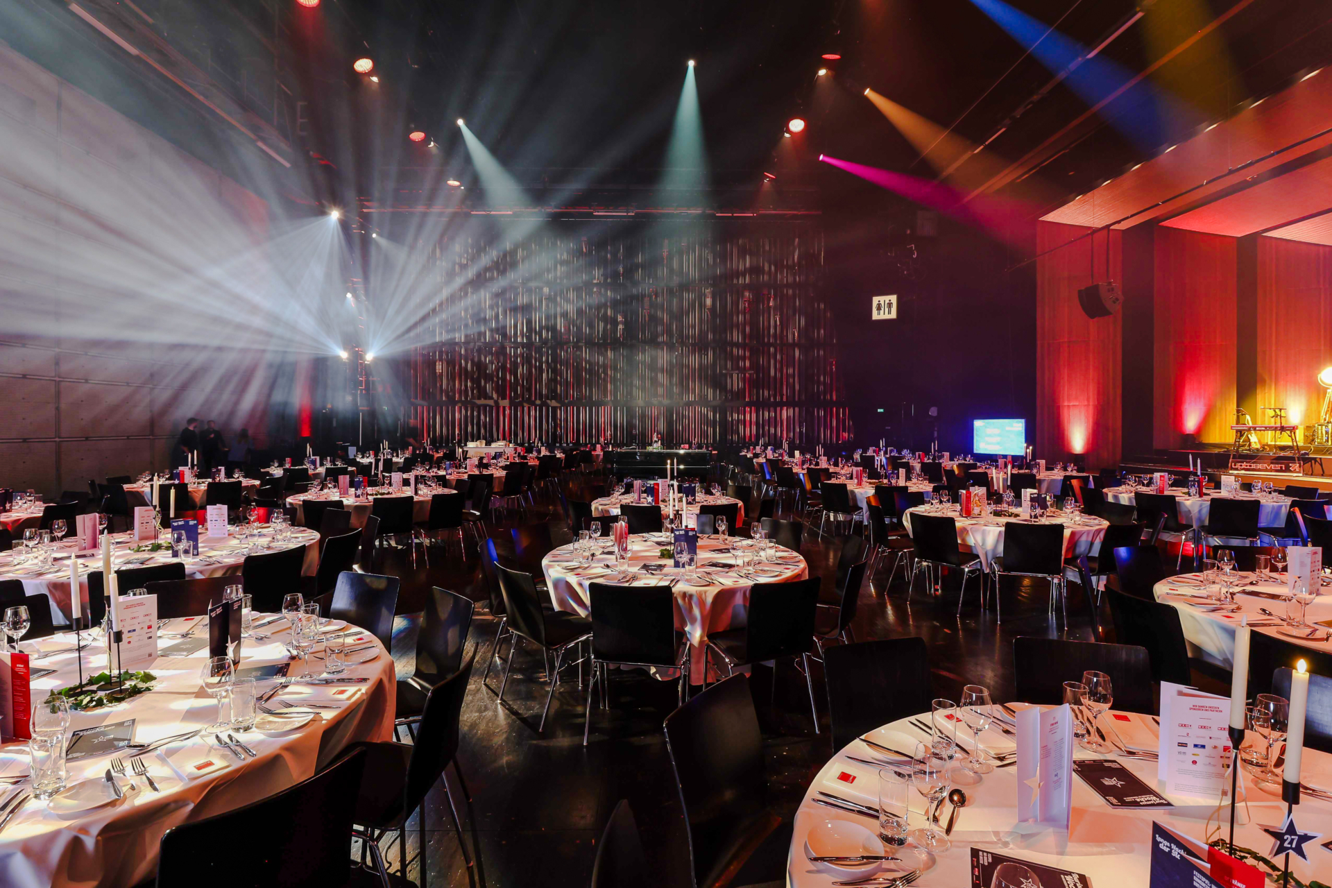 Beleuchteter Veranstaltungsraum mit runden Tischen und Dekoration.