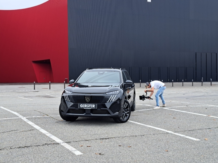 Schwarzes Auto auf Parkplatz, Mann filmt daneben