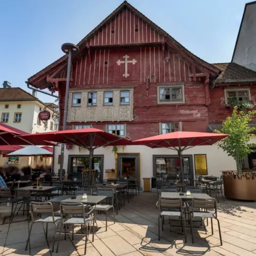 Historisches Gebäude mit Straßencafé und roten Sonnenschirmen