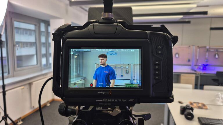 Kamera filmt Person im Arbeitsraum mit Technik.