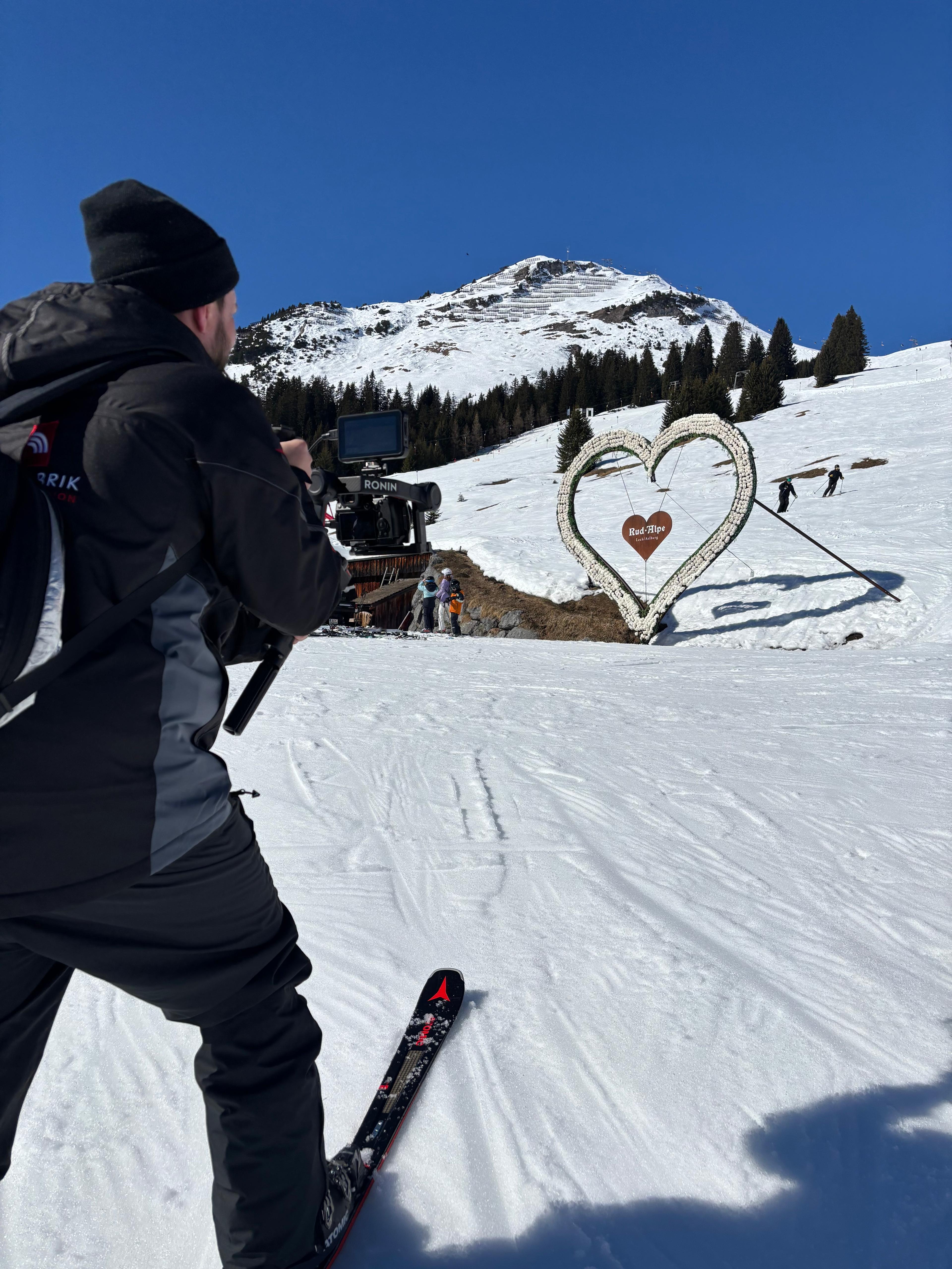 Skifahrer filmt schneebedeckte Berglandschaft mit Herzskulptur.