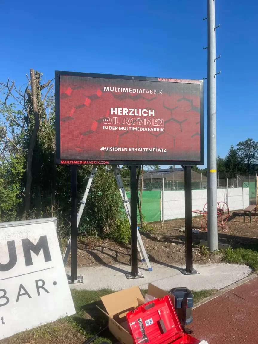 Willkommensschild der MULTIMEDIAFABRIK im Freien aufgestellt.