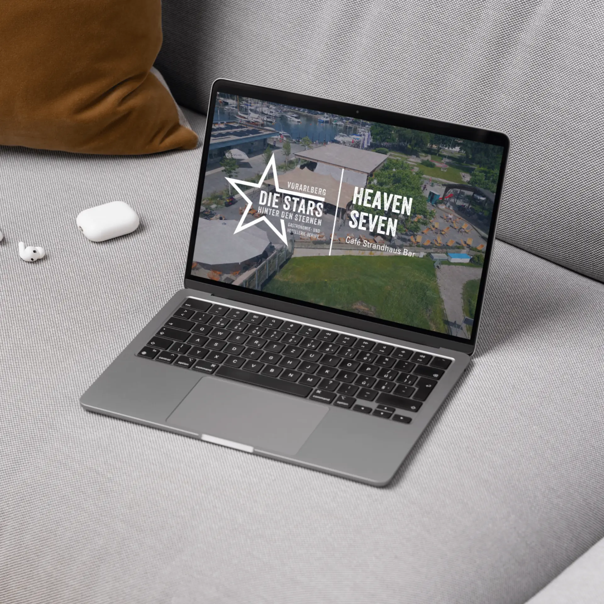 Laptop auf grauem Sofa mit Webseite geöffnet.