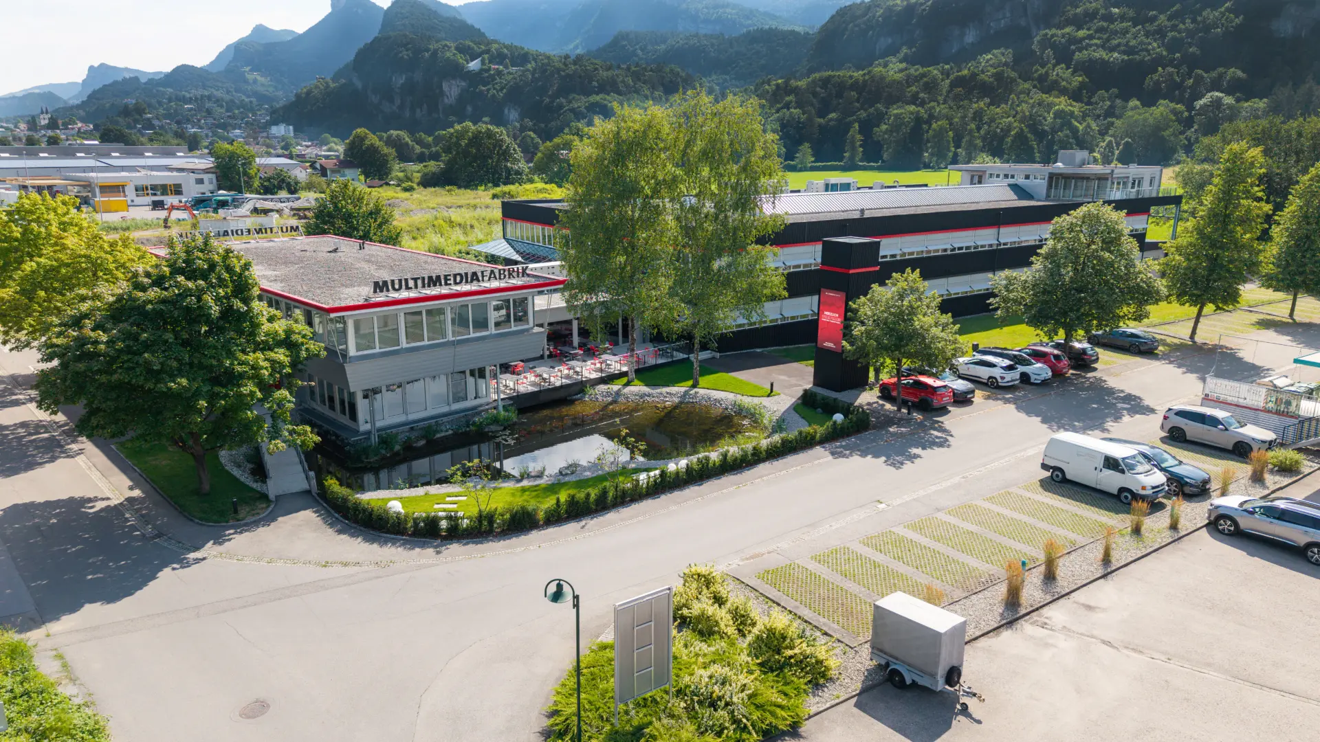 Multimediafabrik mit Parkplatz und Berglandschaft