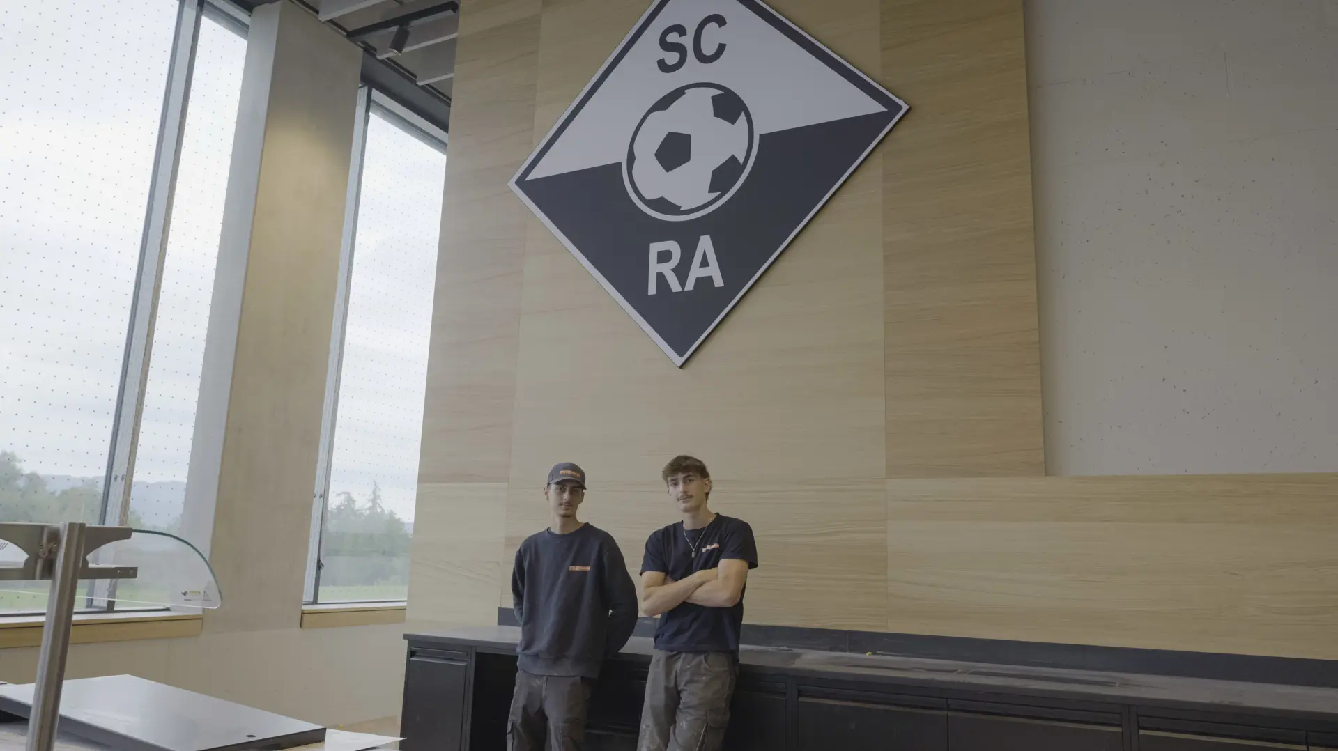 Zwei Personen vor SC RA Logo.