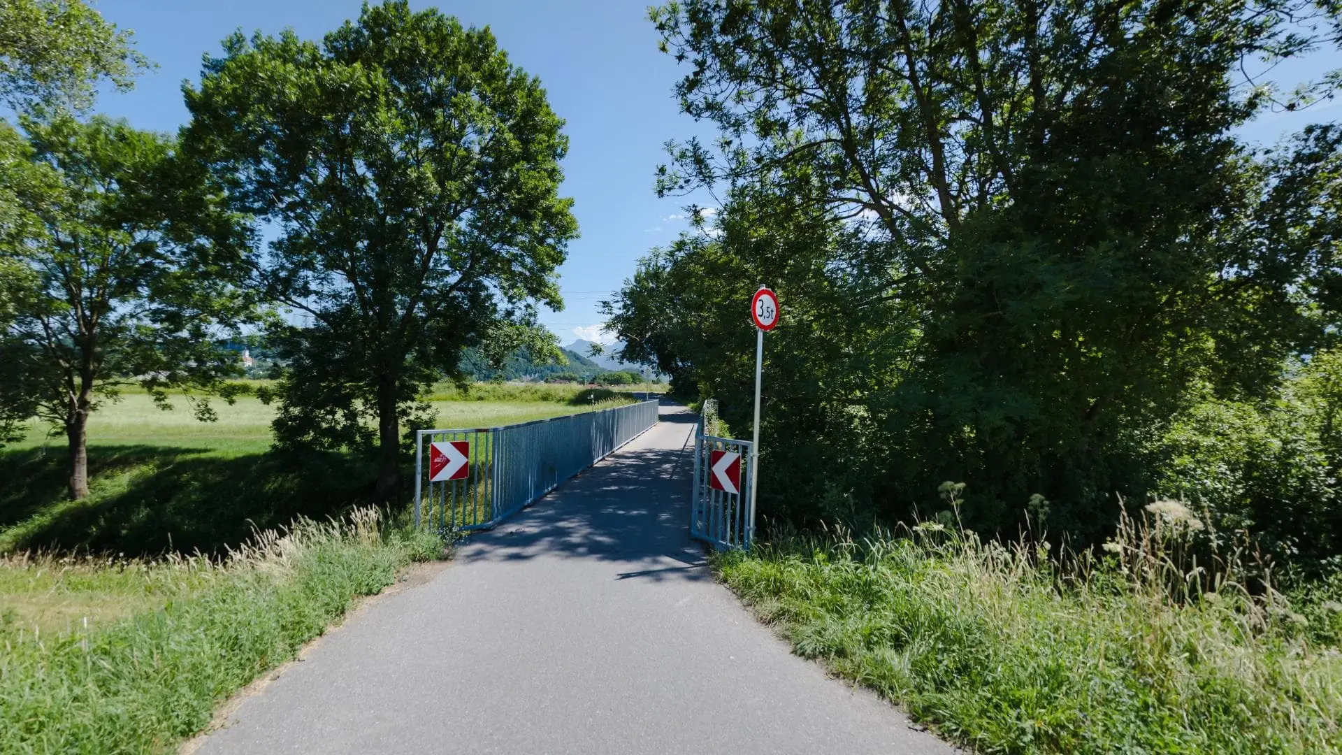 Schmale Brücke mit Bäumen und Verkehrsschild.