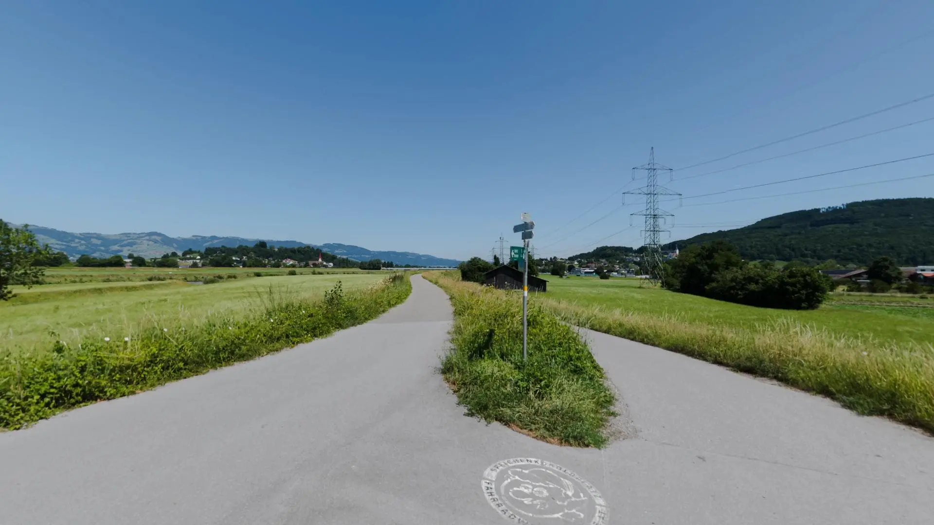 Ländlicher Weg mit Bergblick und Strommast.