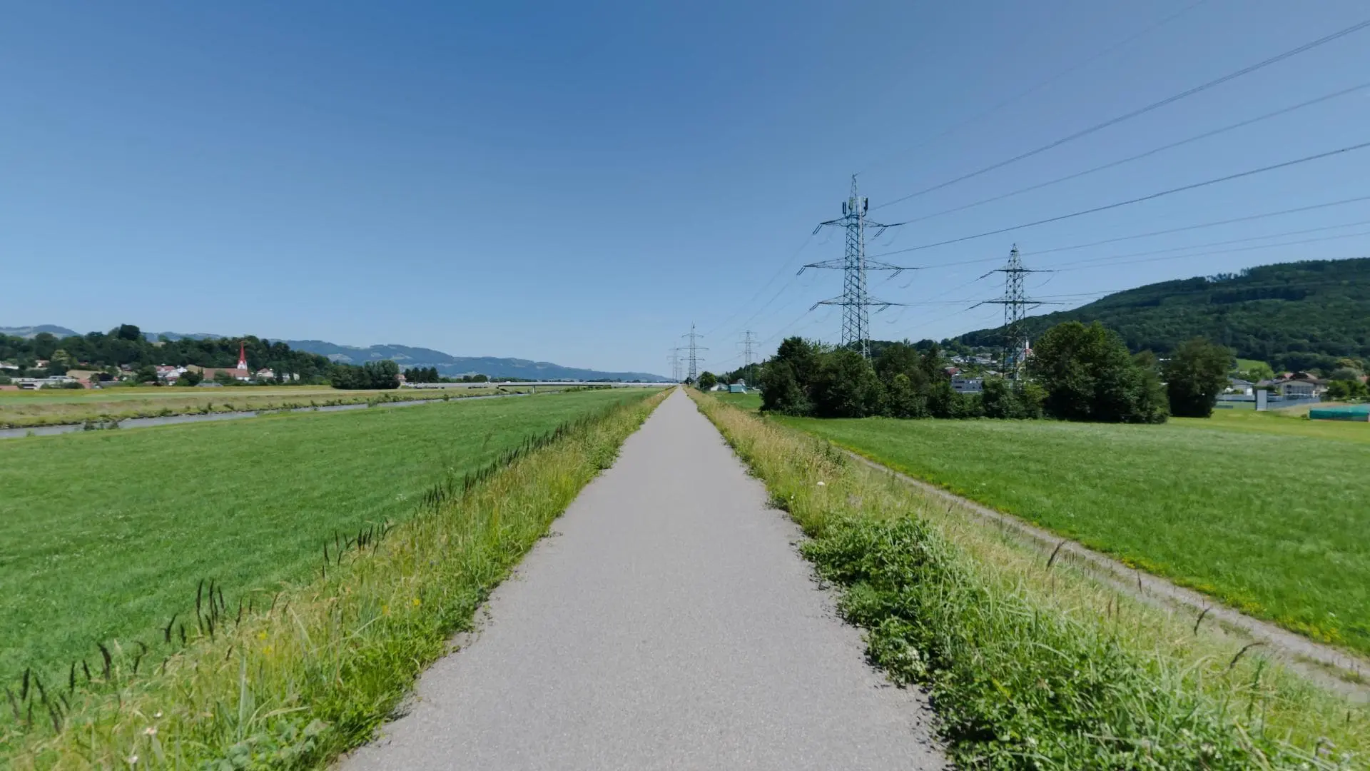 Langer Weg durch grüne Felder und Strommasten.