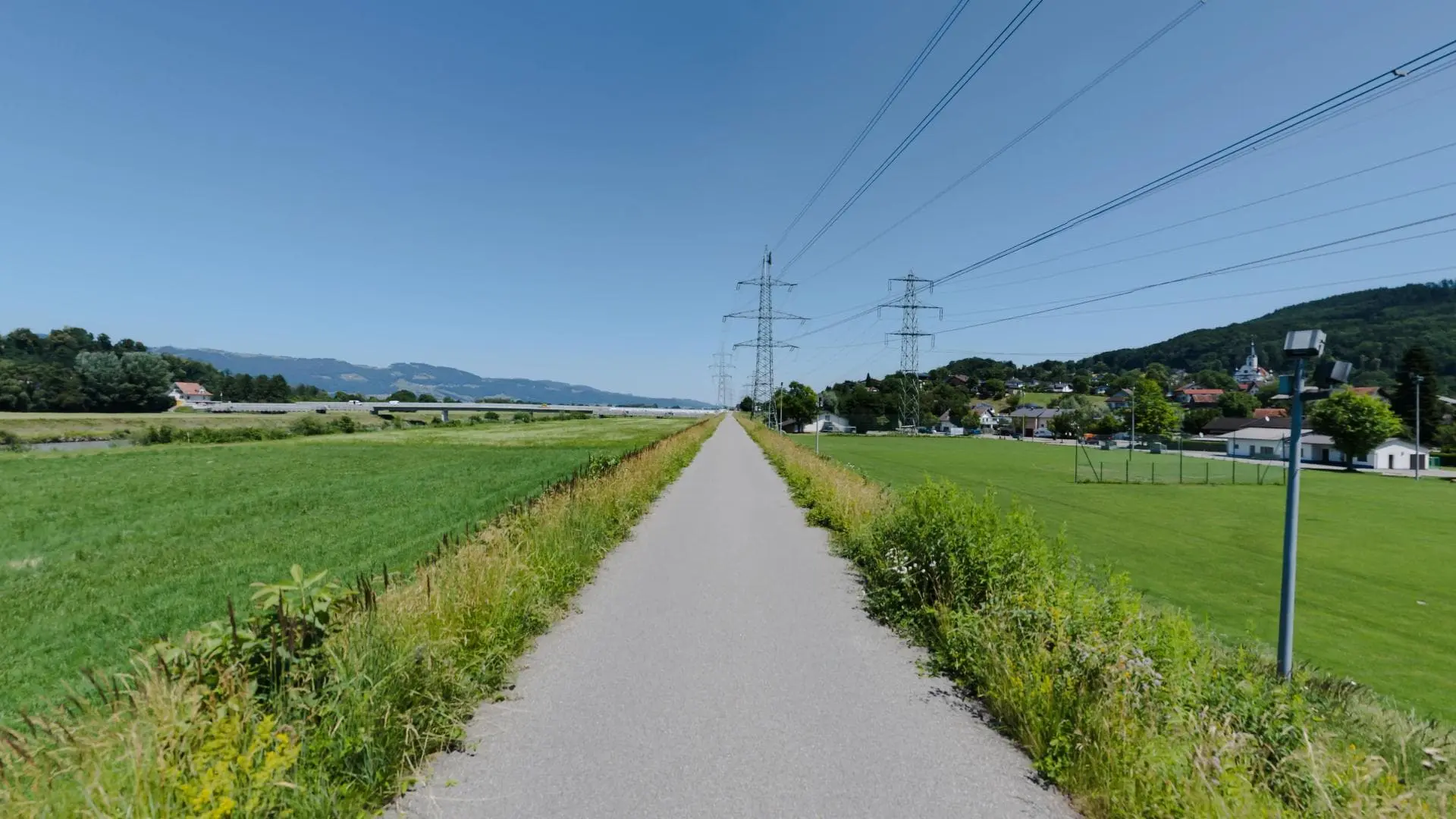 Langer Weg durch grüne Landschaft mit Stromleitungen.