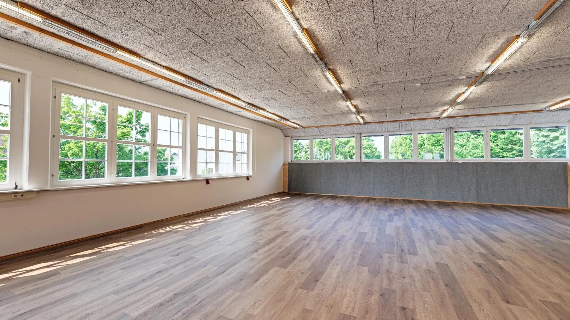 Leerer Raum mit großen Fenstern und Holzboden.