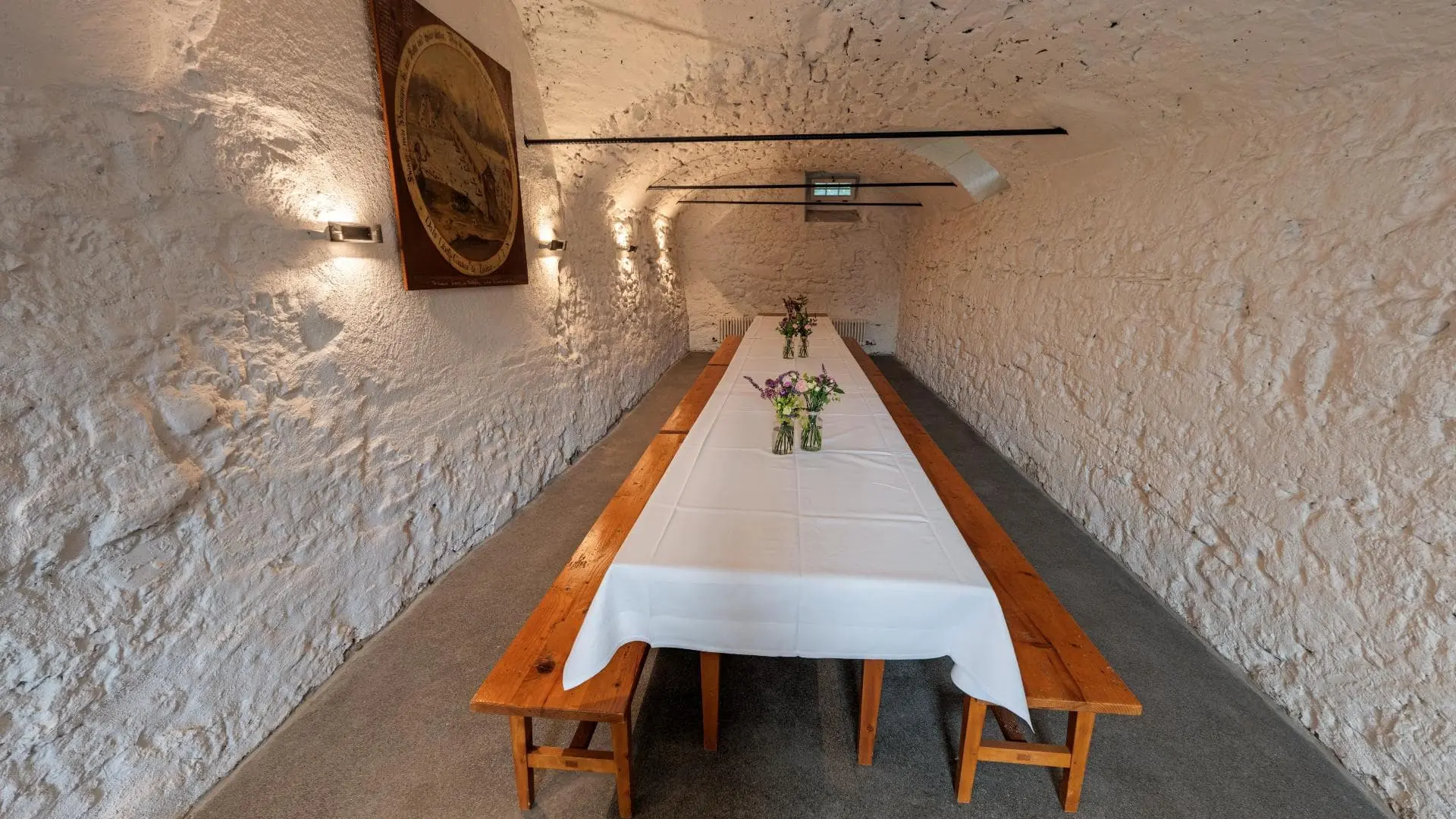 Langer Tisch im rustikalen Raum mit Blumen.