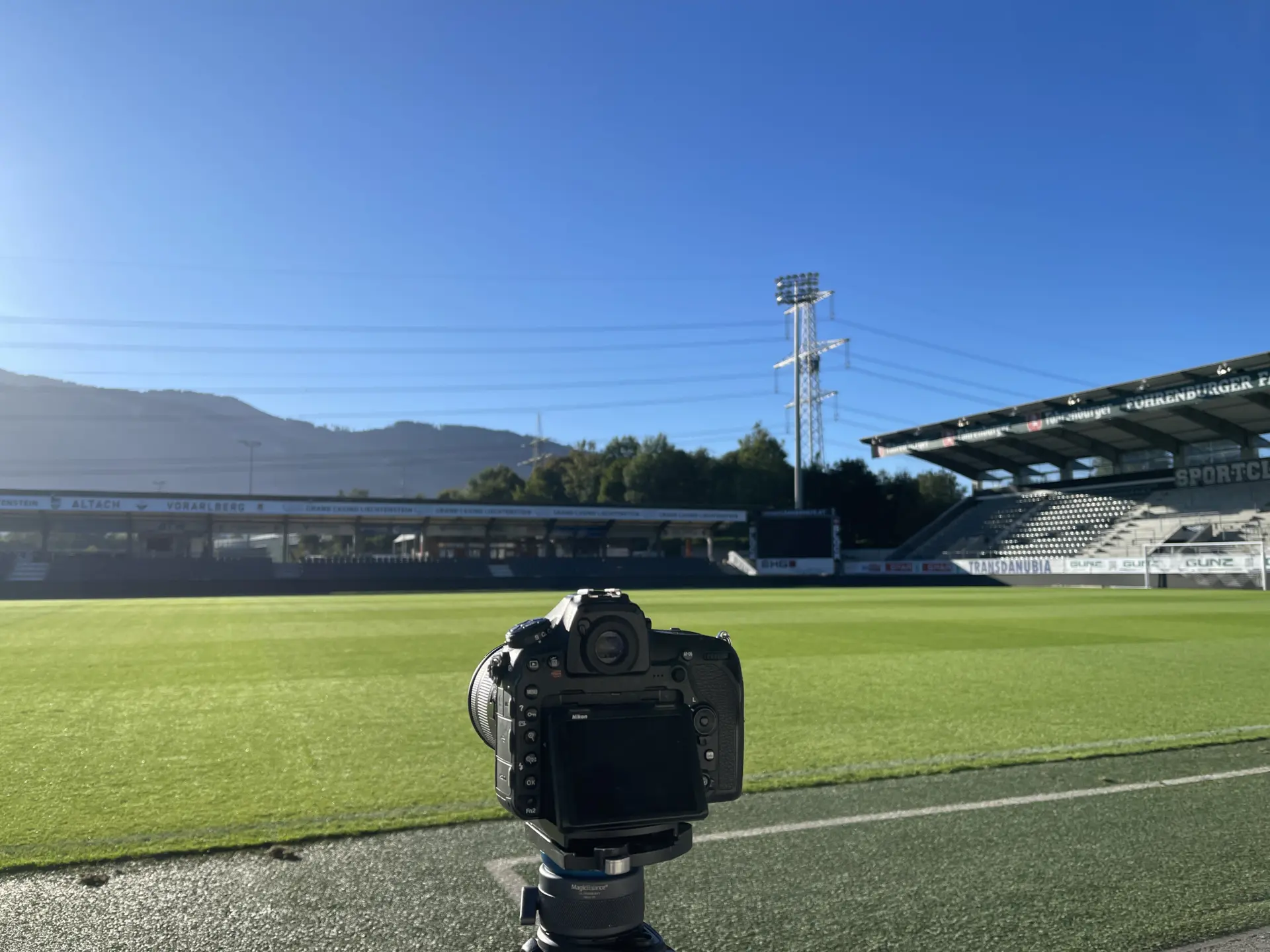 Kamera auf Stativ vor leerem Fußballstadion.