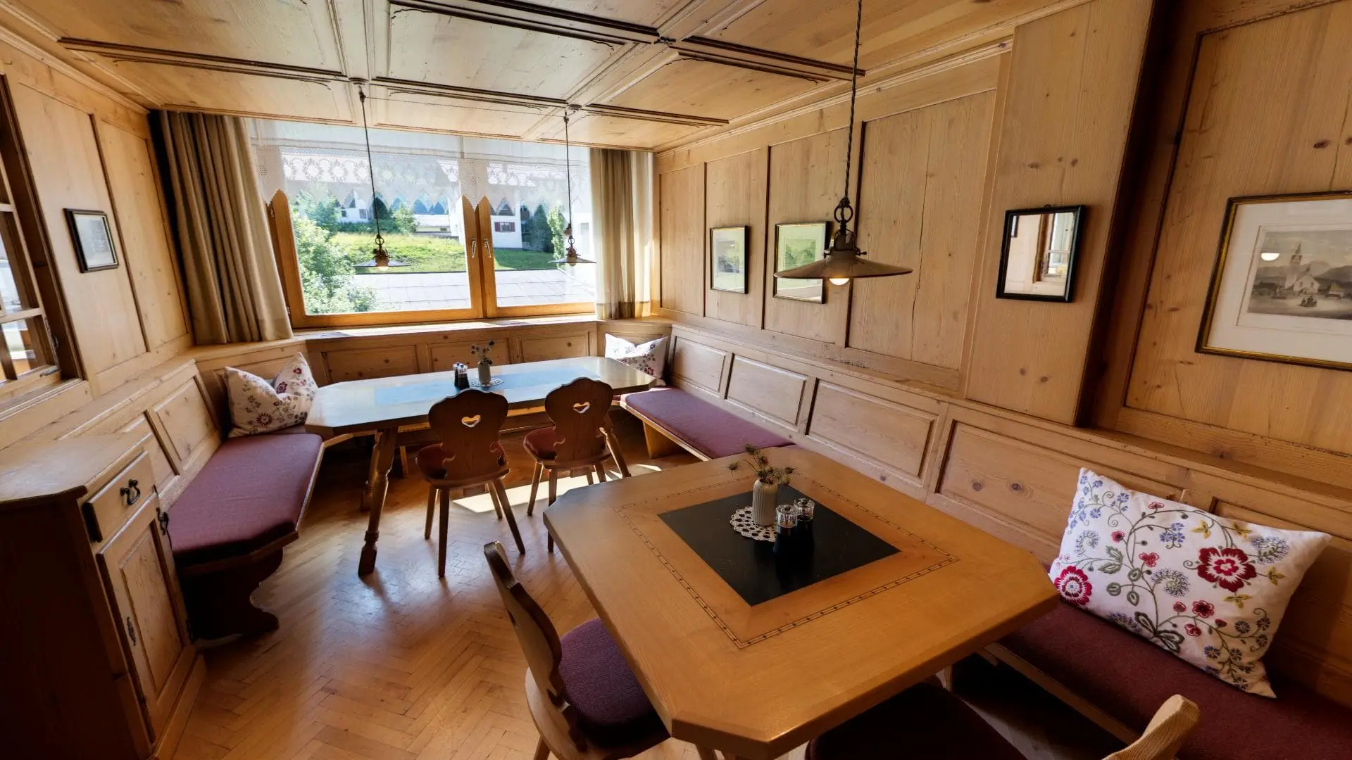 Gemütliche Holzwandstube mit Tischen und Fensterblick.