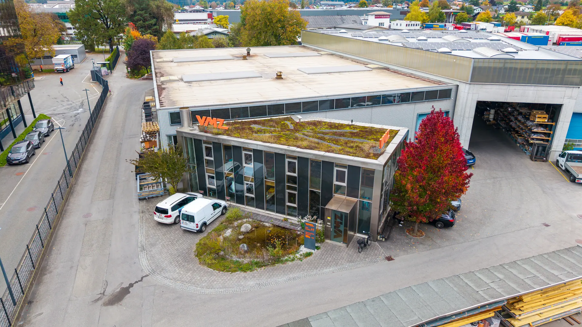 Bürogebäude mit begrüntem Dach und herbstlichen Bäumen.