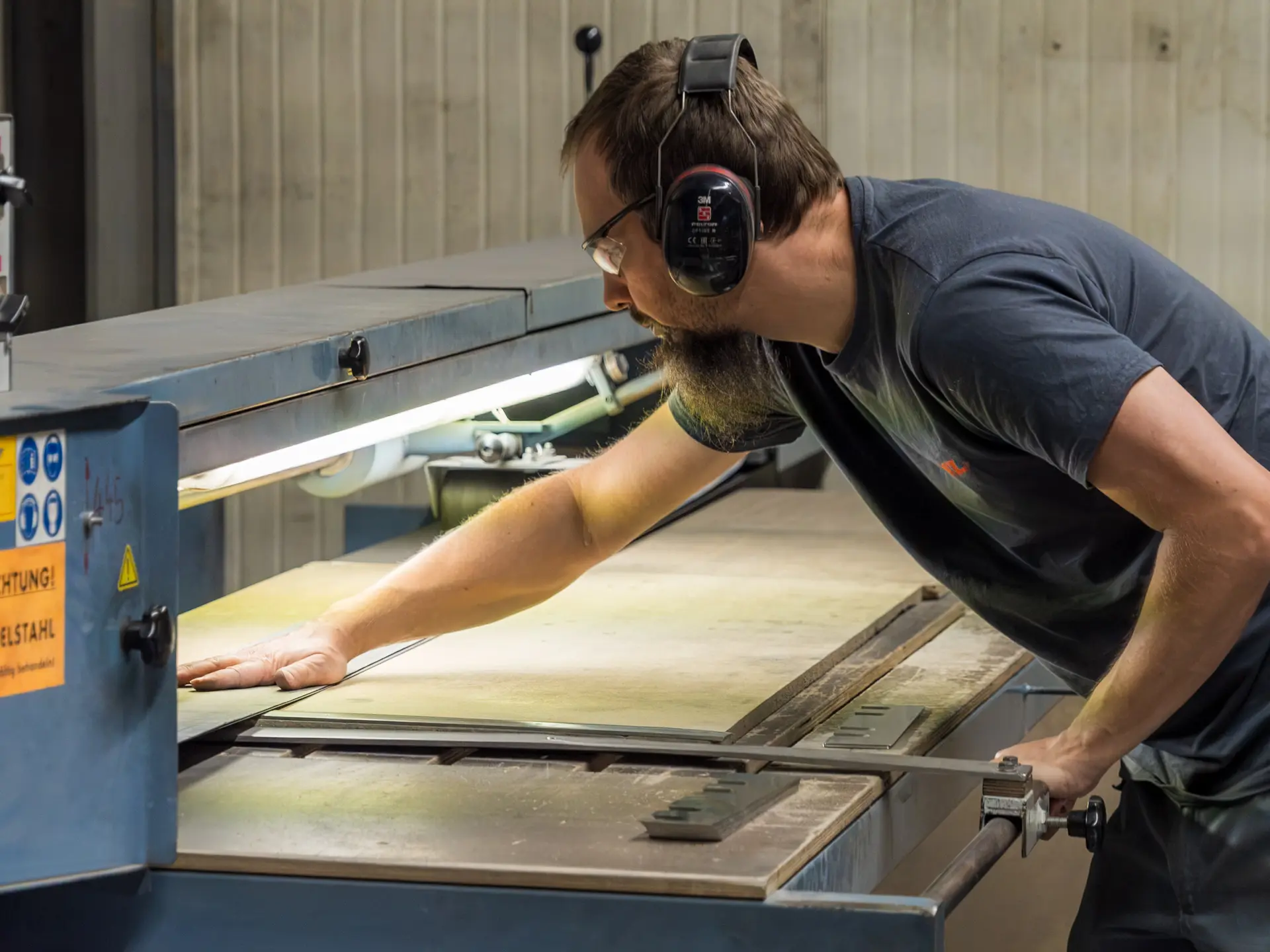 Arbeiter bedient Maschine mit Gehörschutz.