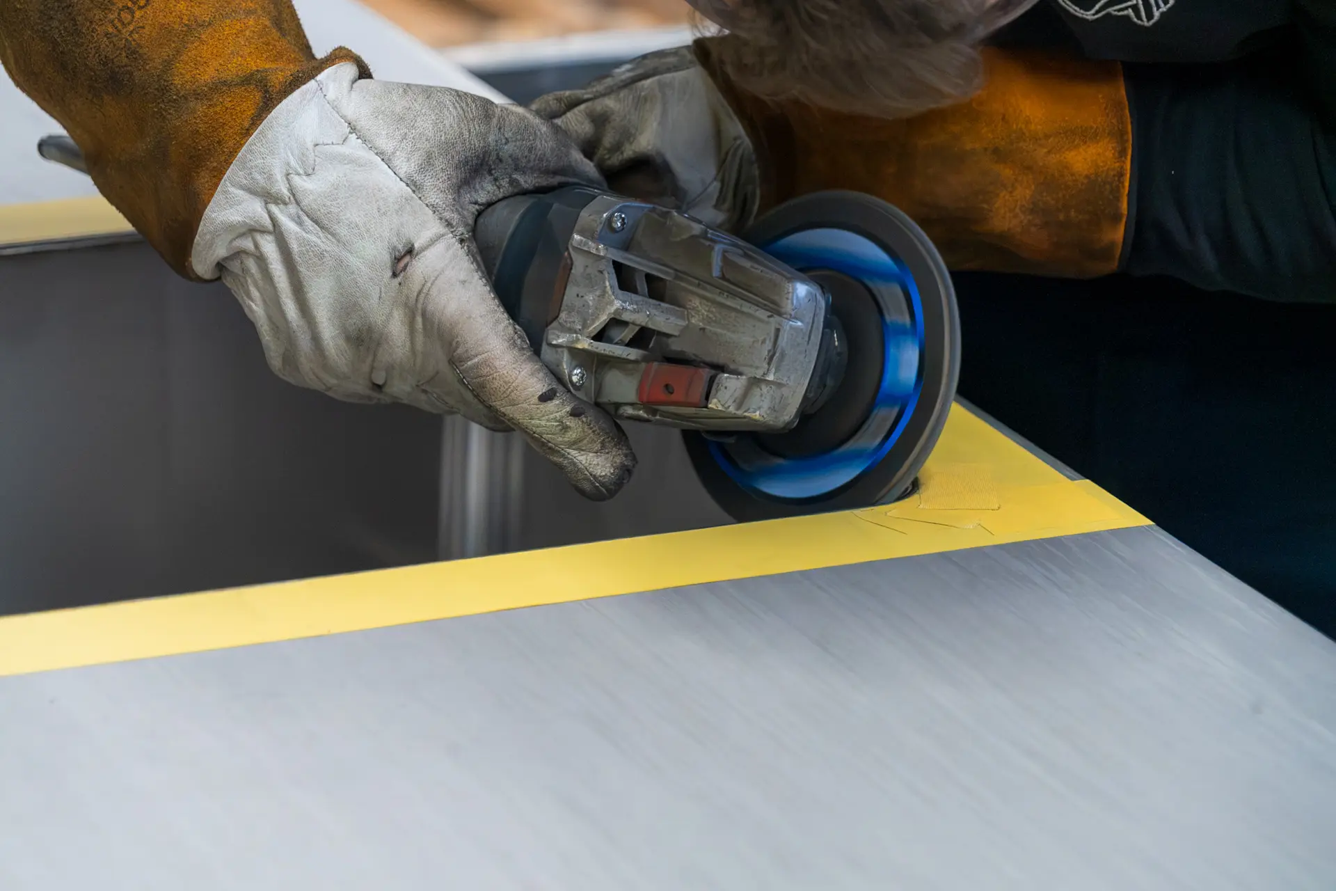 Person schleift Metall mit Winkelschleifer ab.