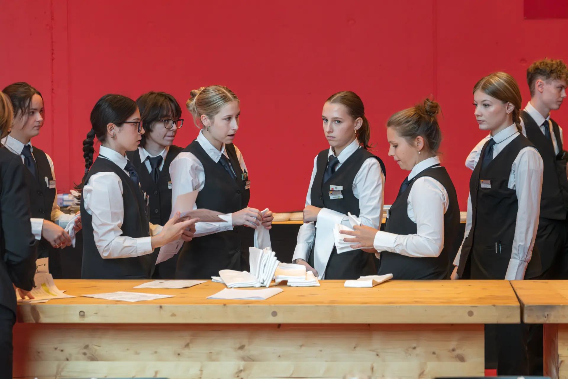 Junge Leute in Uniform falten Servietten an einem Tisch.