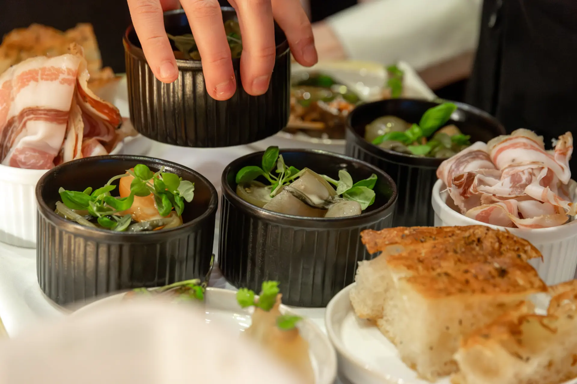Hand greift nach Vorspeisen in schwarzen Schalen.
