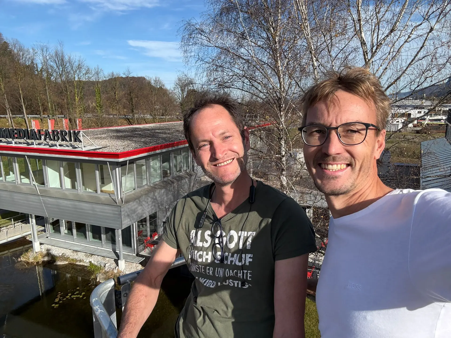 Zwei Männer vor einem Gebäude mit Mediafabrik-Logo.