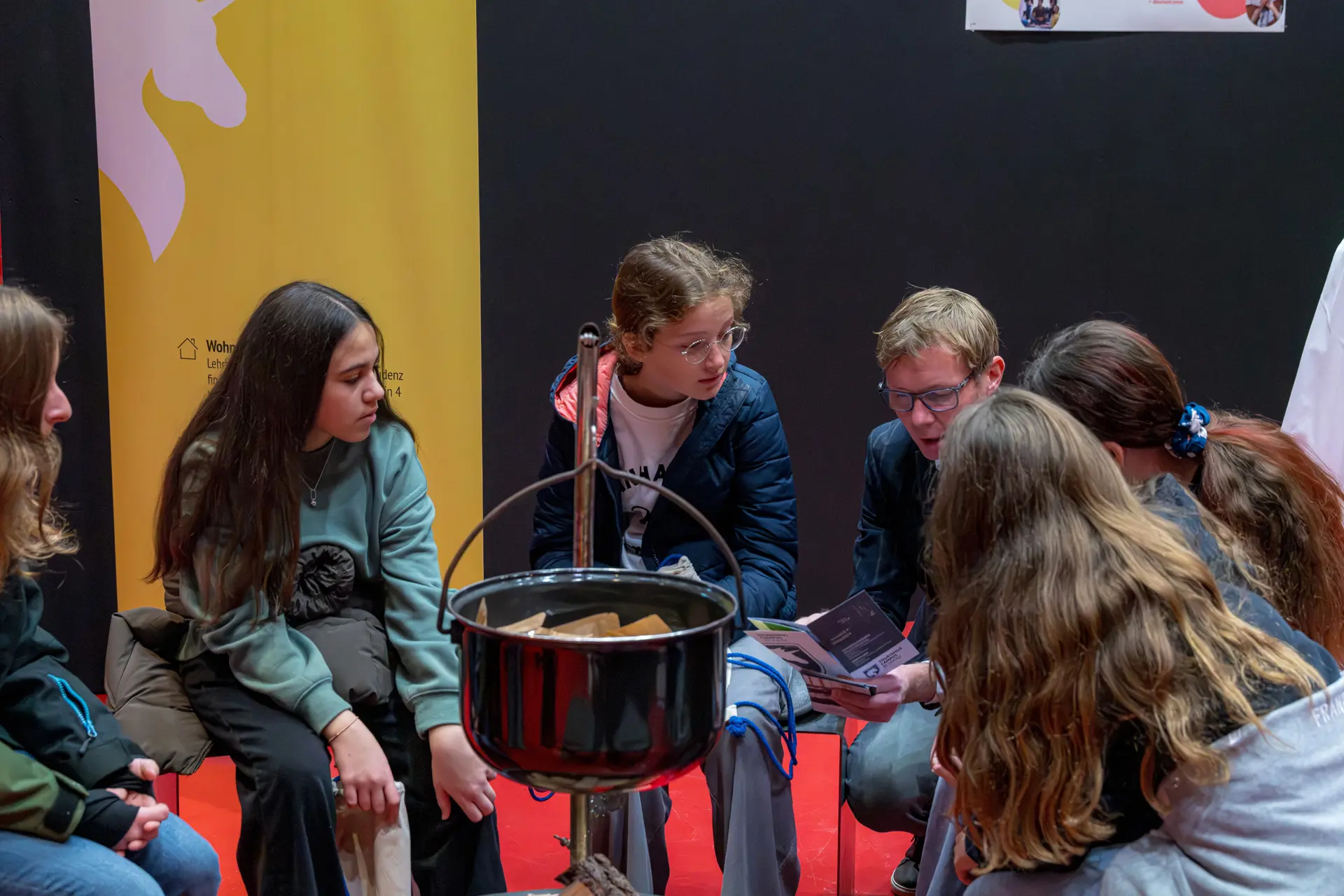 Gruppe junger Leute sitzt um einen Kessel.