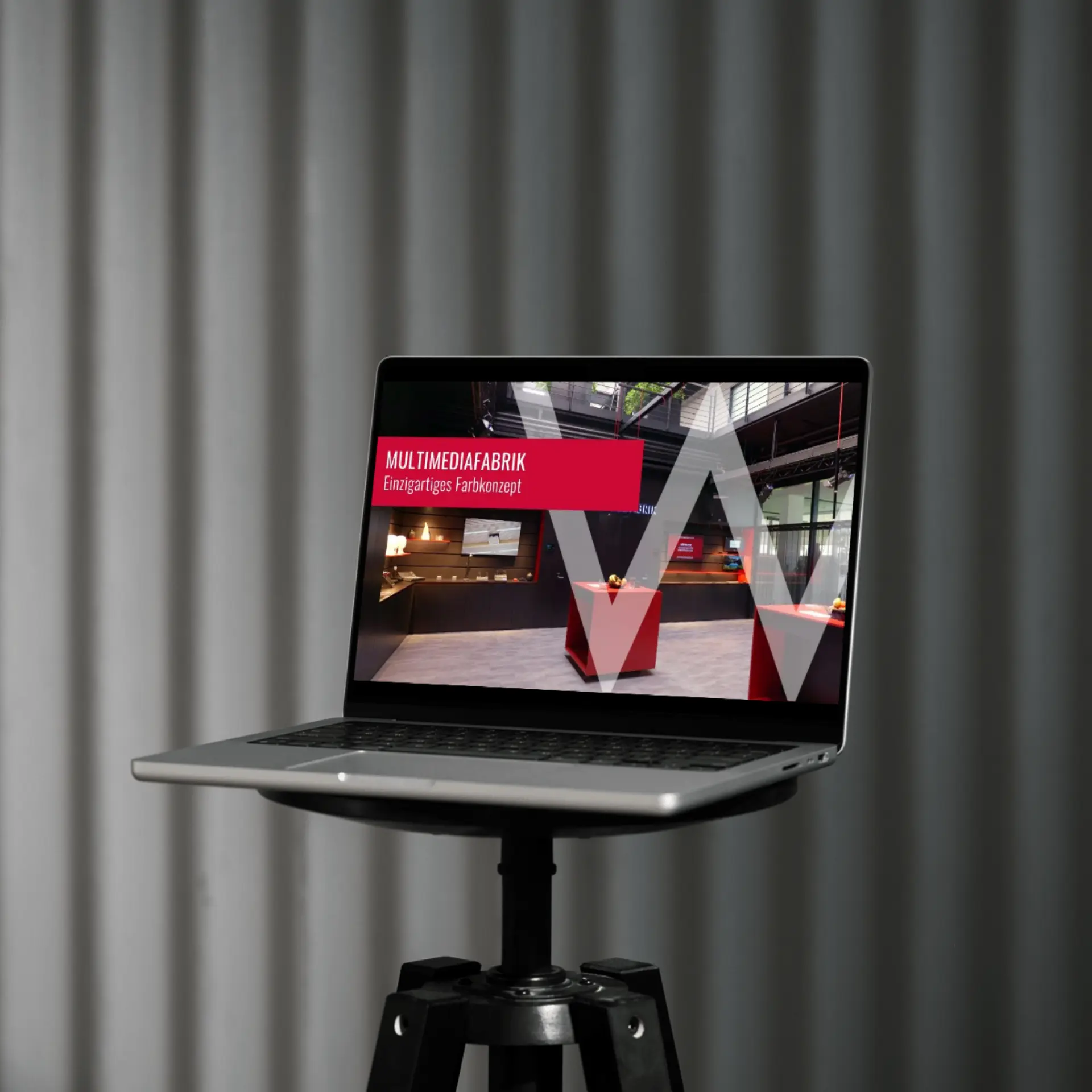 Laptop mit Startseite von Multimediafabrik auf Stativ.