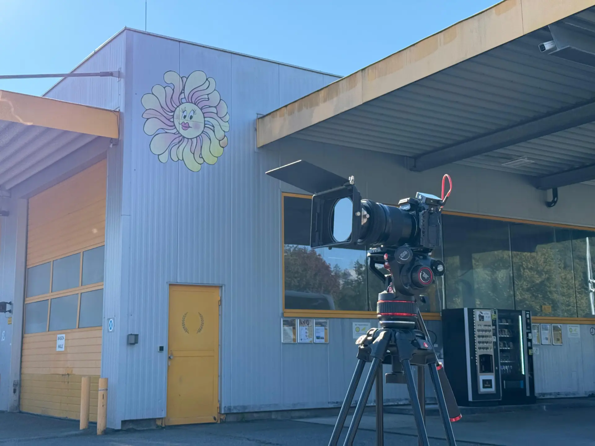 Kamera auf Stativ vor Industriegebäude mit Blumengraffiti.