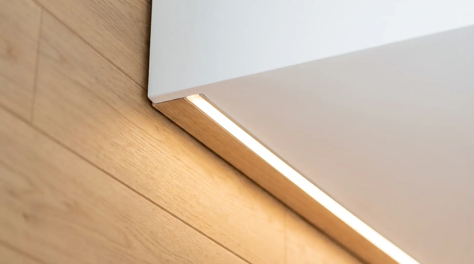 Nahaufnahme einer präzise gebauten Schattenfuge mit durchgehender warmer LED-Linie zwischen Decke und Eichenwand