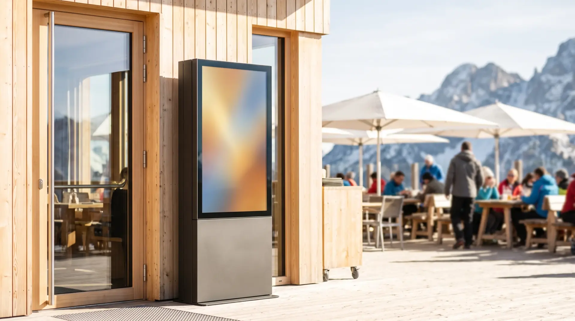 Wetterfeste Stele im Hochformat neben dem Eingang eines Restaurants mit Terrasse und Bergen im Hintergrund