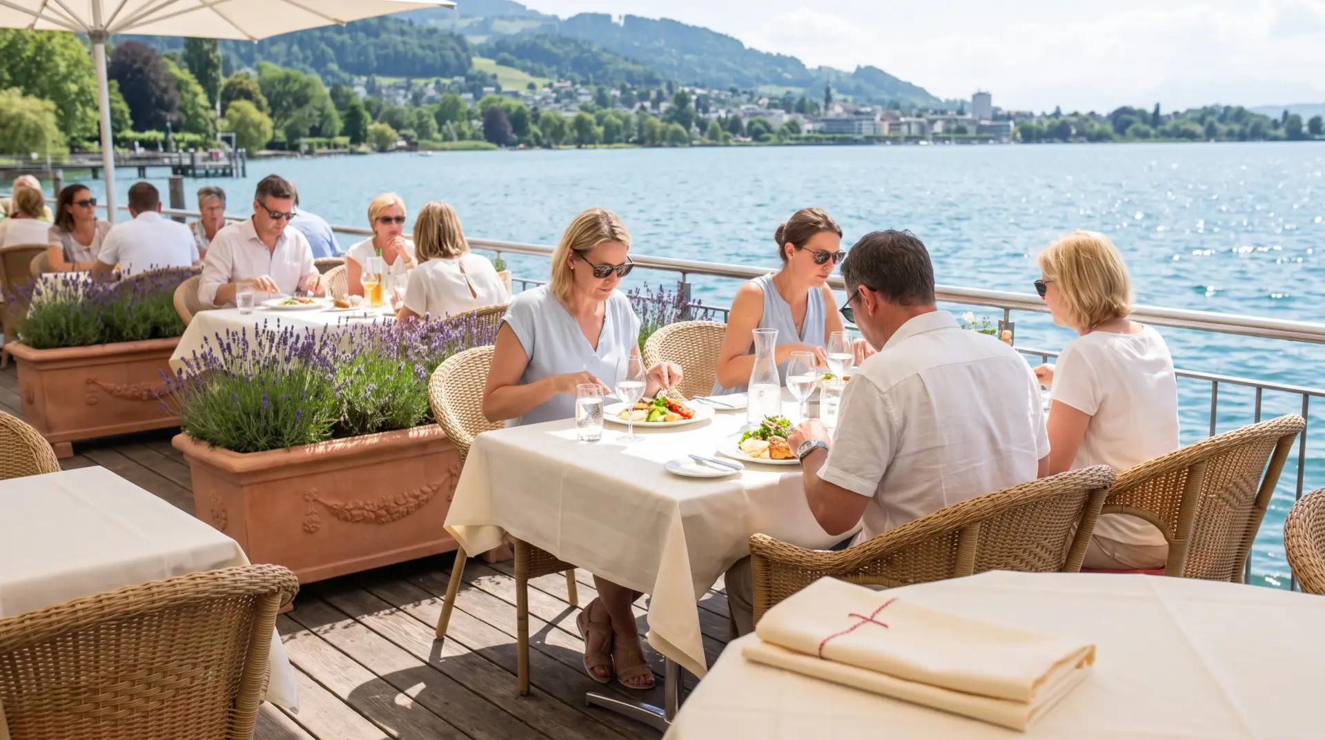 Sonnige Restaurantterrasse am Bodensee mit gedeckten Tischen, Gästen beim Mittagessen und Blick auf See und Hügel