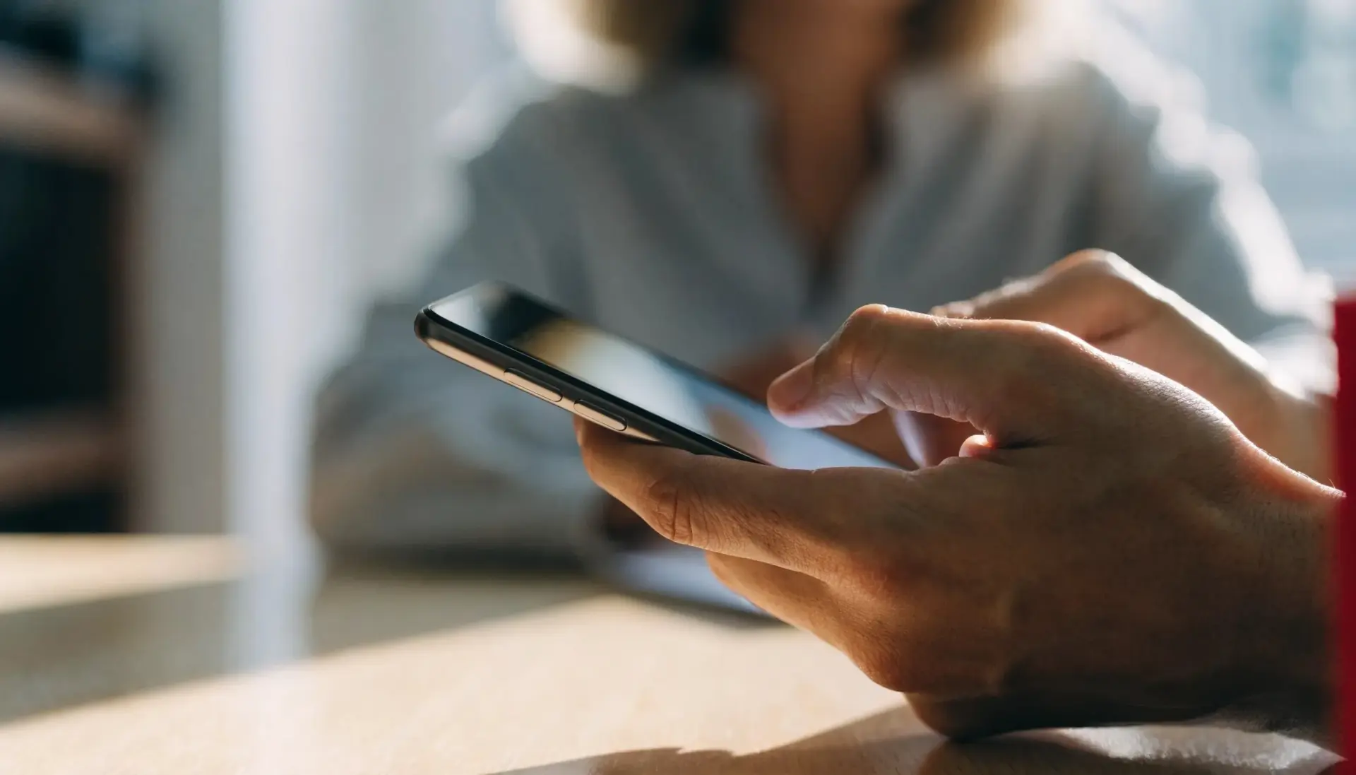 Funnel KI APP: Nahaufnahme von Händen mit Smartphone über einem Schreibtisch (MULTIMEDIAFABRIK, Koblach, Vorarlberg)
